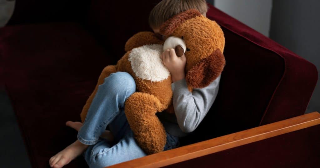 A boy hugging his teddy bear and hiding behind it https://www.autismparentingmagazine.com/autism-and-hoarding/