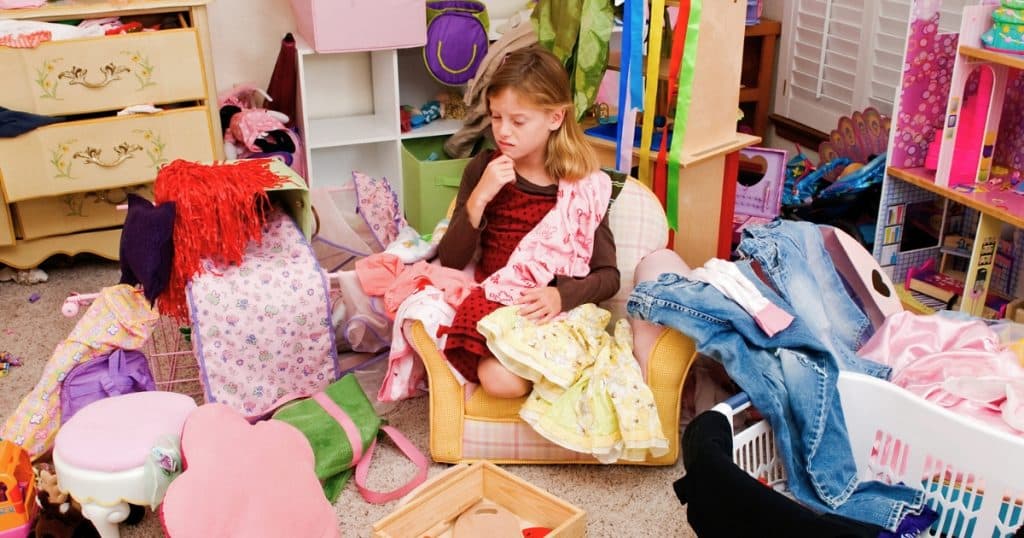 Little girl sitting in a messy room full of clothes https://www.autismparentingmagazine.com/autism-and-hoarding/