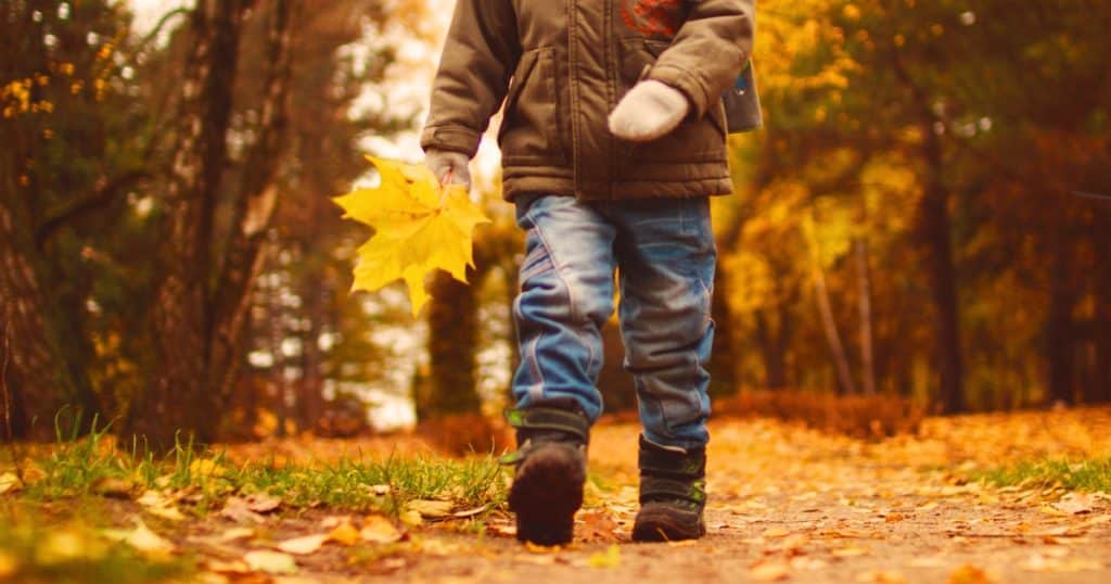 Child walking outside in fall and carrying a yellow leaf https://www.autismparentingmagazine.com/fall-sensory-activities/