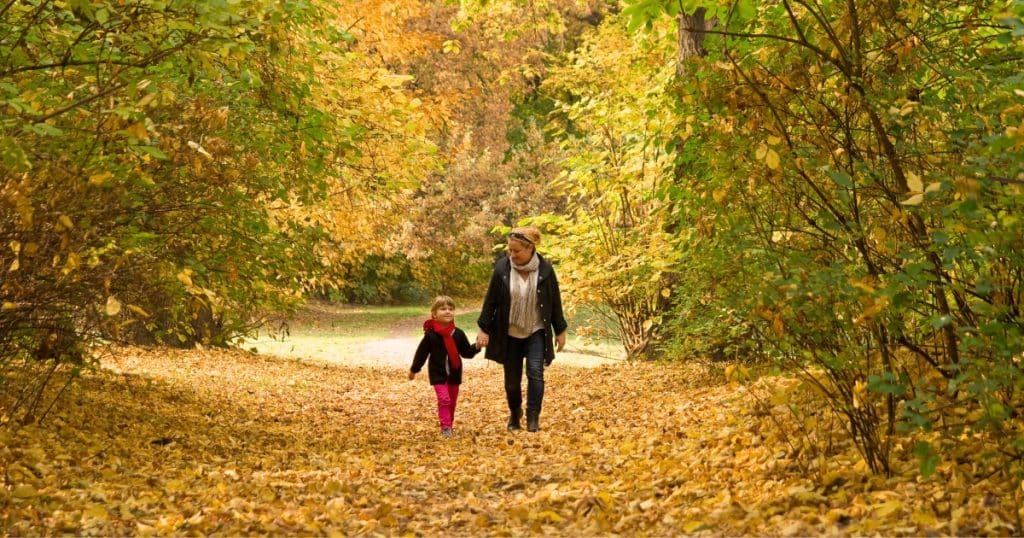 Mom and daughter walking through the woods in the fall https://www.autismparentingmagazine.com/fall-sensory-activities/