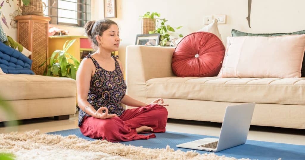 Girl meditating in her home with a laptop in front of her https://www.autismparentingmagazine.com/meditation-for-autism/